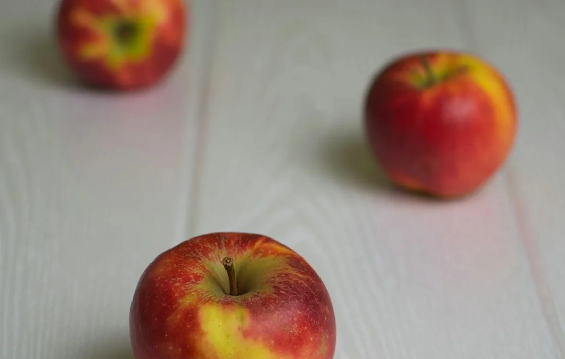 Three red apples on a light wooden surface, with a shallow depth of field and blurred background.