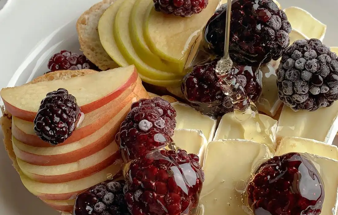 Plate with sliced apples and blackberries arranged with a few cheese wedges.