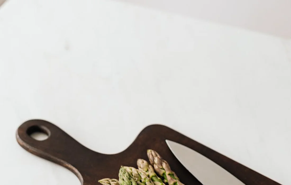 Fresh asparagus spears arranged on a dark wooden cutting board on a white surface.
