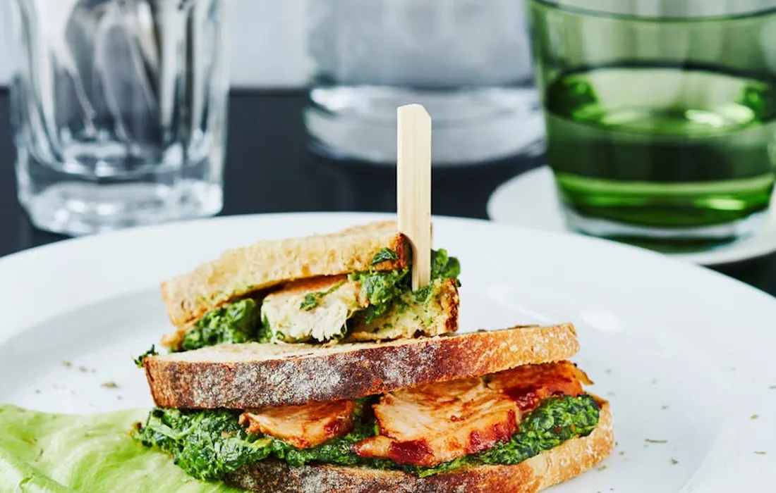 Crusty bread stacked into a small sandwich with greens, held together by a wooden skewer on a white plate.