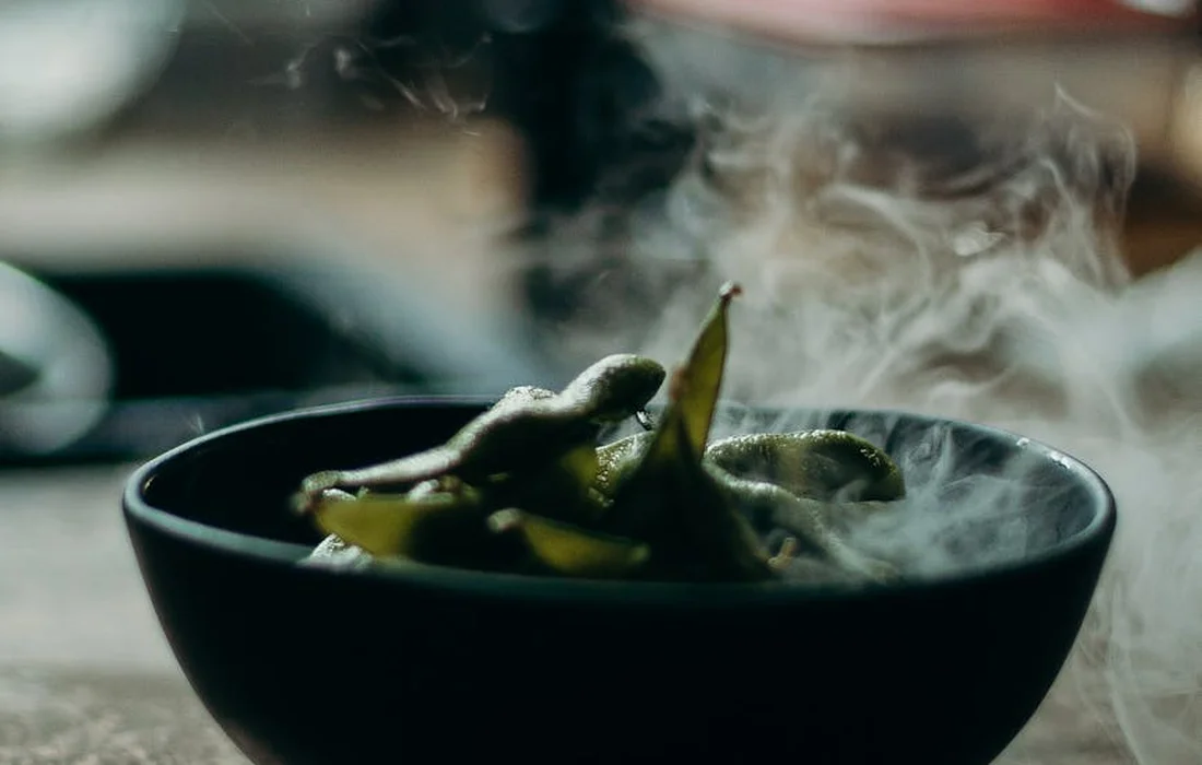 Steaming green beans in a black bowl on a wooden surface.