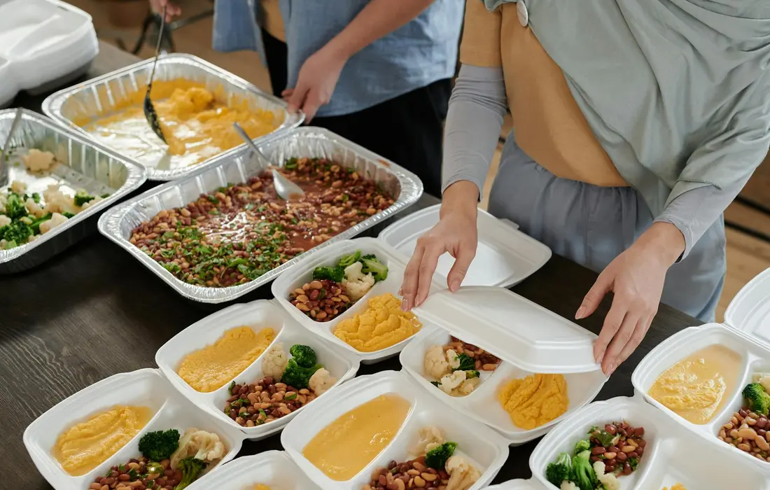 People serving a variety of bean dishes from aluminum trays onto bowls, illustrating a meal setup with beans and vegetables.