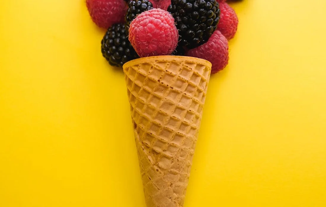Waffle cone filled with blackberries and raspberries on a bright yellow background