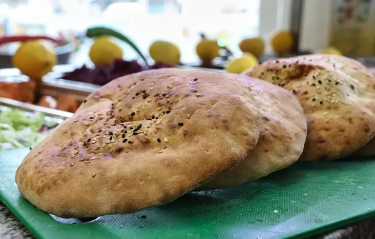 Close-up of two bagels on a green cutting board with a blurred market background featuring lemons and other produce.