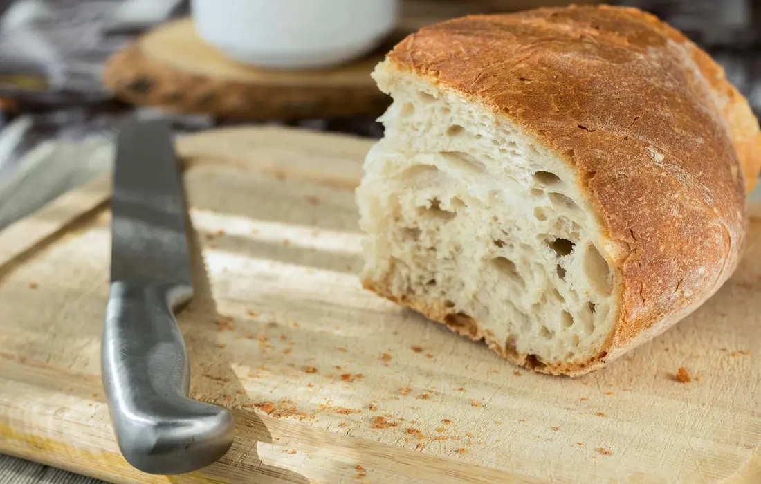 Crusty loaf of bread on a wooden cutting board with a knife beside it
