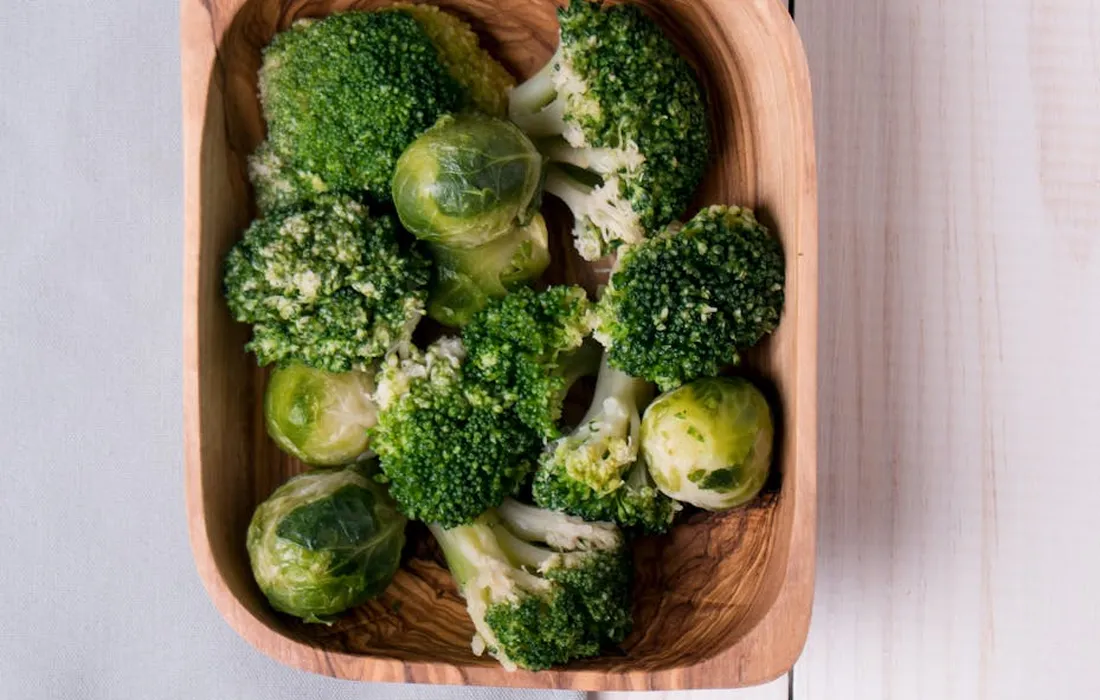 Fresh broccoli florets in a wooden basket on a light surface.