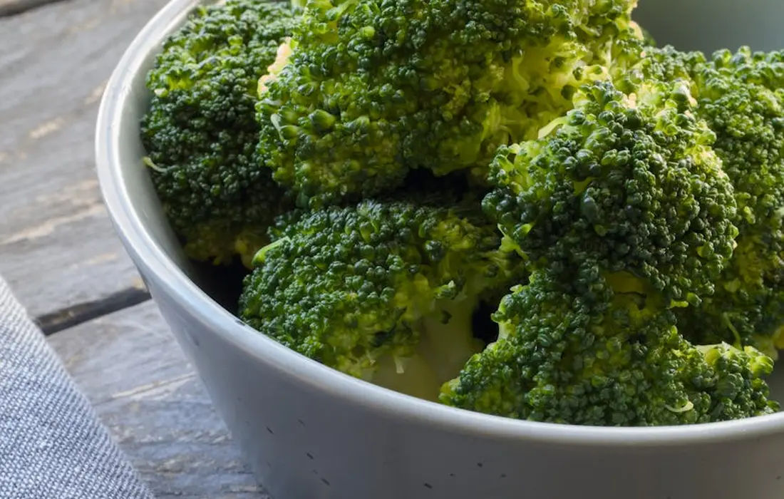 Fresh broccoli florets in a light gray bowl on a wooden surface.