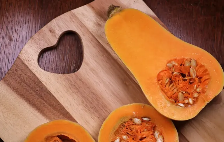 Halved butternut squash on a wooden cutting board with the orange flesh and seeds visible