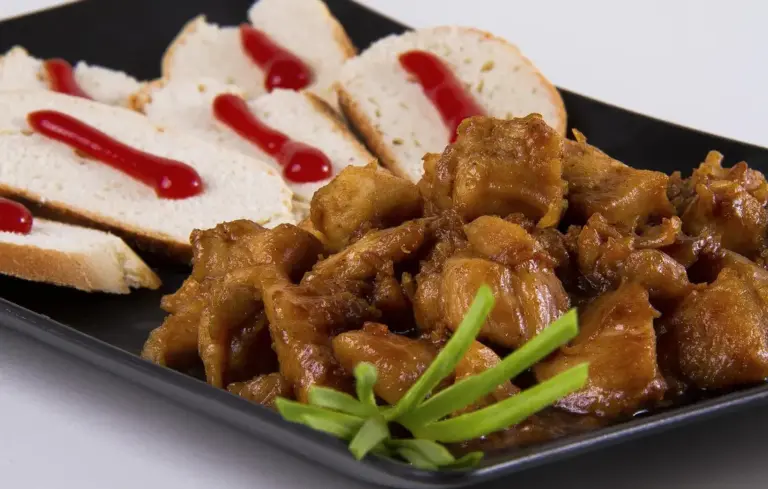 Cooked meat chunks on a black plate with sliced bread and a green garnish