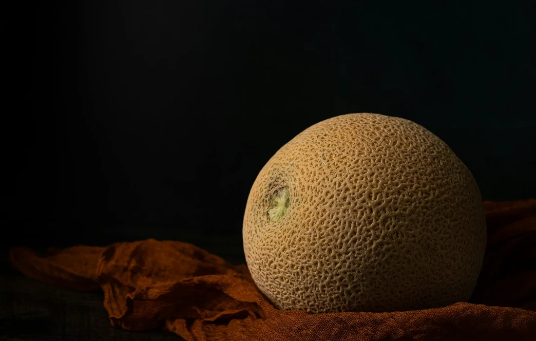 A ripe cantaloupe resting on a rustic brown cloth against a dark background