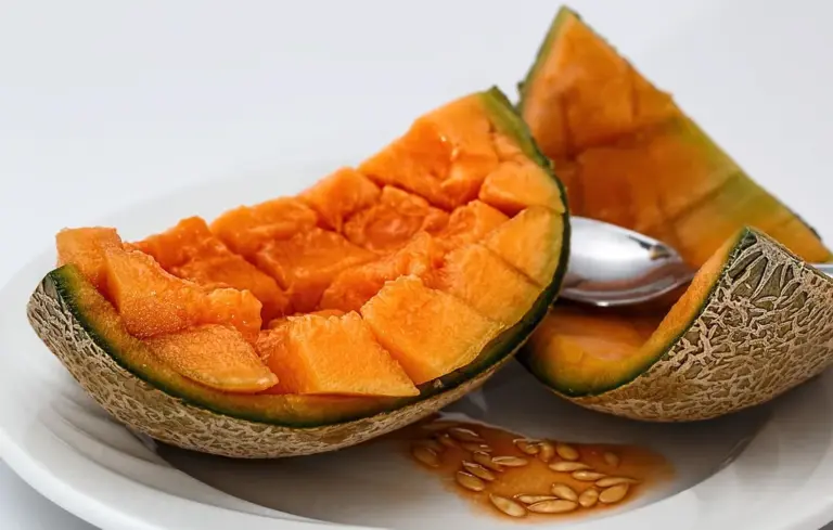 Two halves of cantaloupe with orange flesh cut into chunks on a white plate, with seeds visible.
