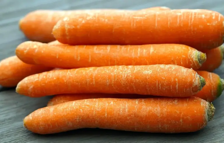 Pile of fresh orange carrots stacked on a wooden surface