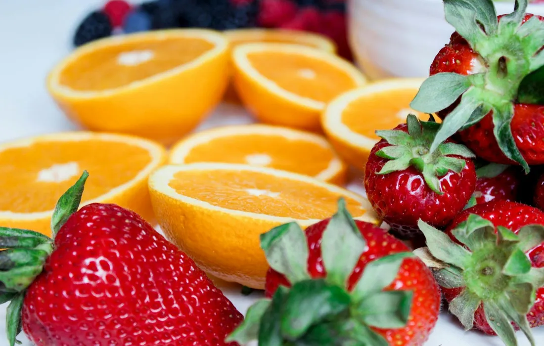 Close-up of fresh strawberries and halved oranges on a white surface, illustrating berry treats for cattle.