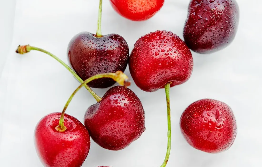 Close-up of fresh red cherries with water droplets on a white background, some with stems attached