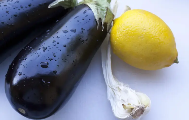 Eggplants with garlic and a lemon on a light surface, illustrating eggplant as a potential component of a chicken diet.