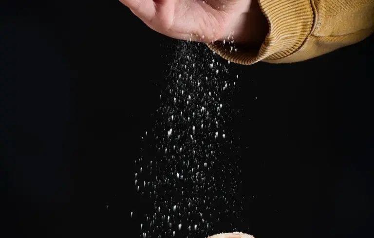 Close-up of a hand sprinkling white granules (salt) onto a surface against a dark background