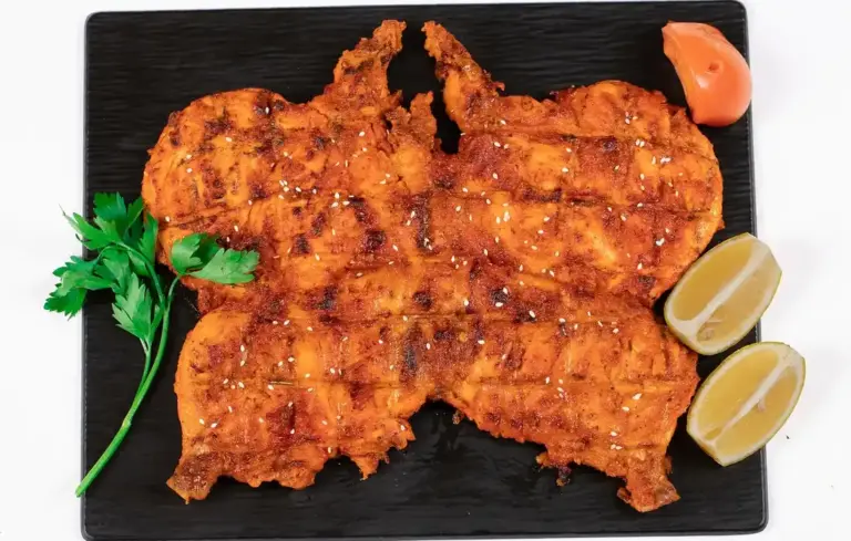 Crispy fried chicken on a black rectangular plate with lemon wedges and a sprig of parsley.