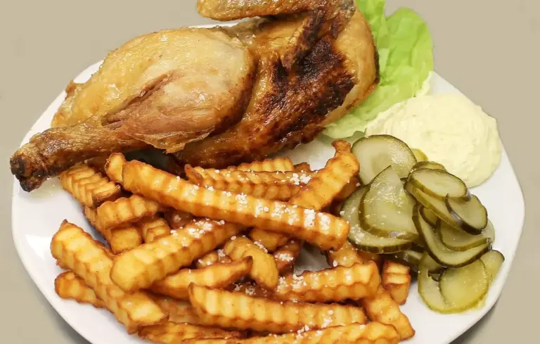 Plate with roasted chicken leg, crinkle-cut fries, pickle slices, lettuce, and mashed potatoes.