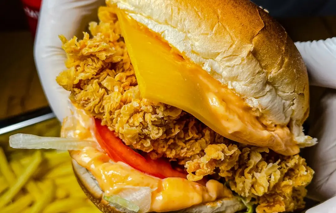 Close-up of a fried chicken sandwich with melted cheese and a tomato slice on a bun.