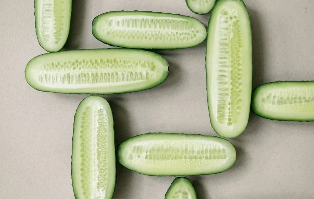 Several cucumber slices and sticks arranged on a light gray background
