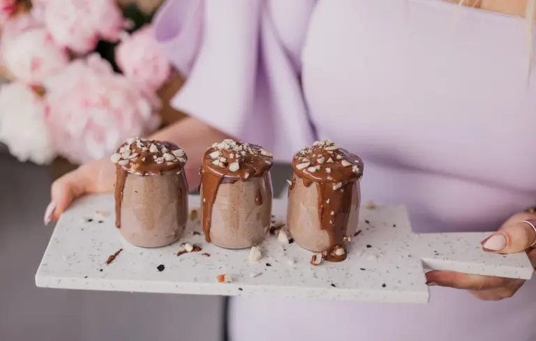 Three chocolate cupcakes with frosting and sprinkles on a speckled white serving board, held by a person in a lavender top