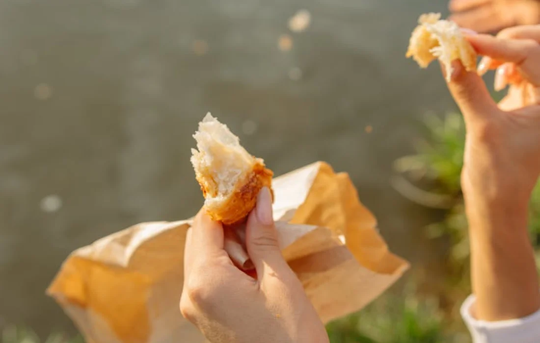 Two hands tearing a piece of bread to feed ducks by a pond