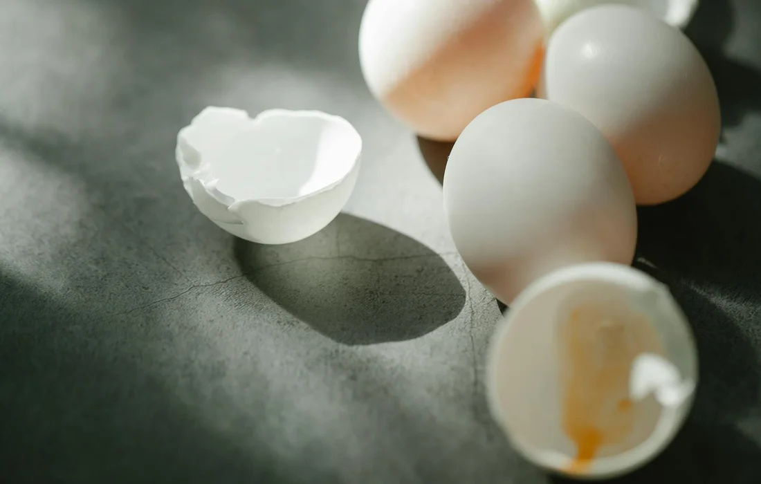 Several eggs, including a cracked eggshell, on a dark, textured surface.