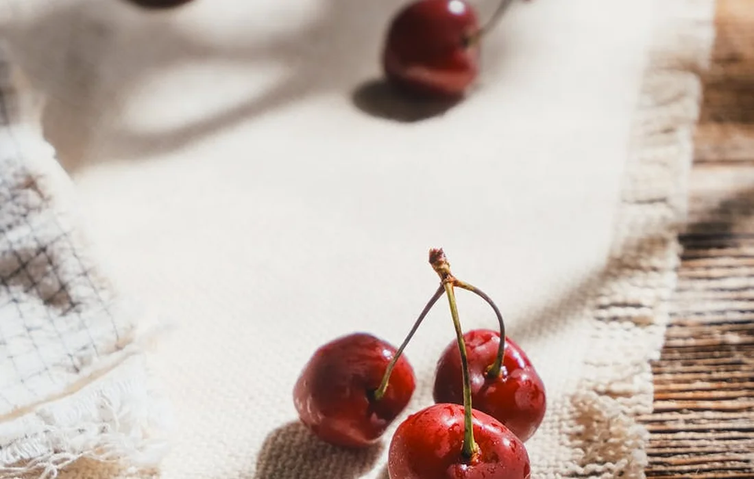 Close-up of fresh red cherries on a light fabric background, illustrating fruit treats for chickens.