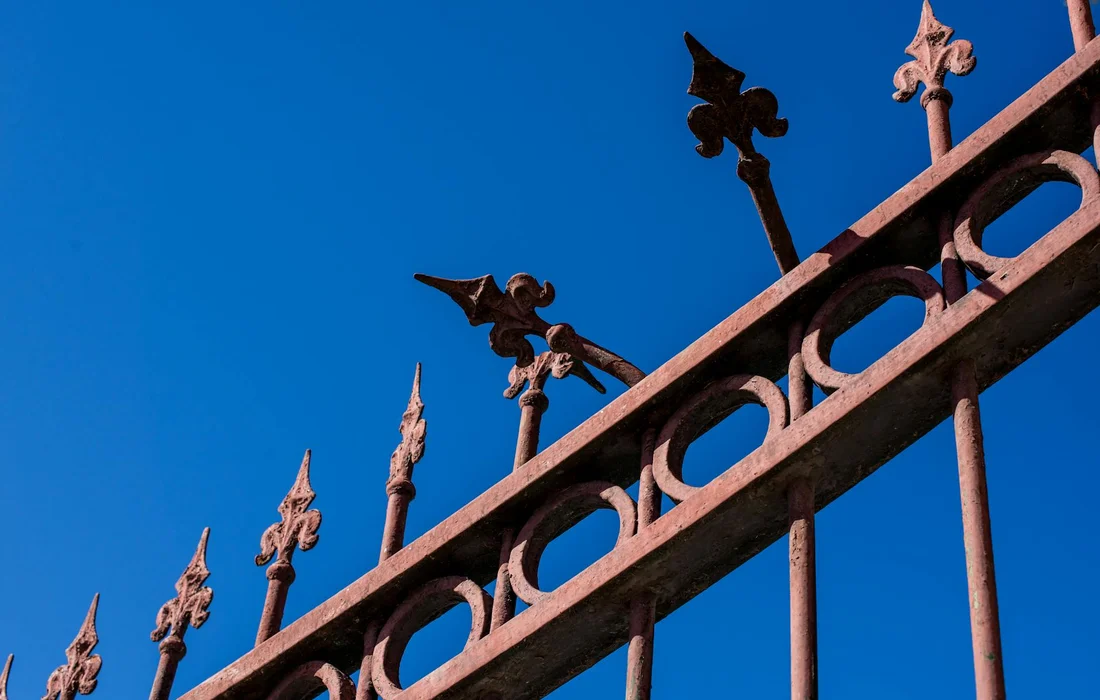 Close-up of a wrought-iron garden fence with decorative spear-like finials against a clear blue sky