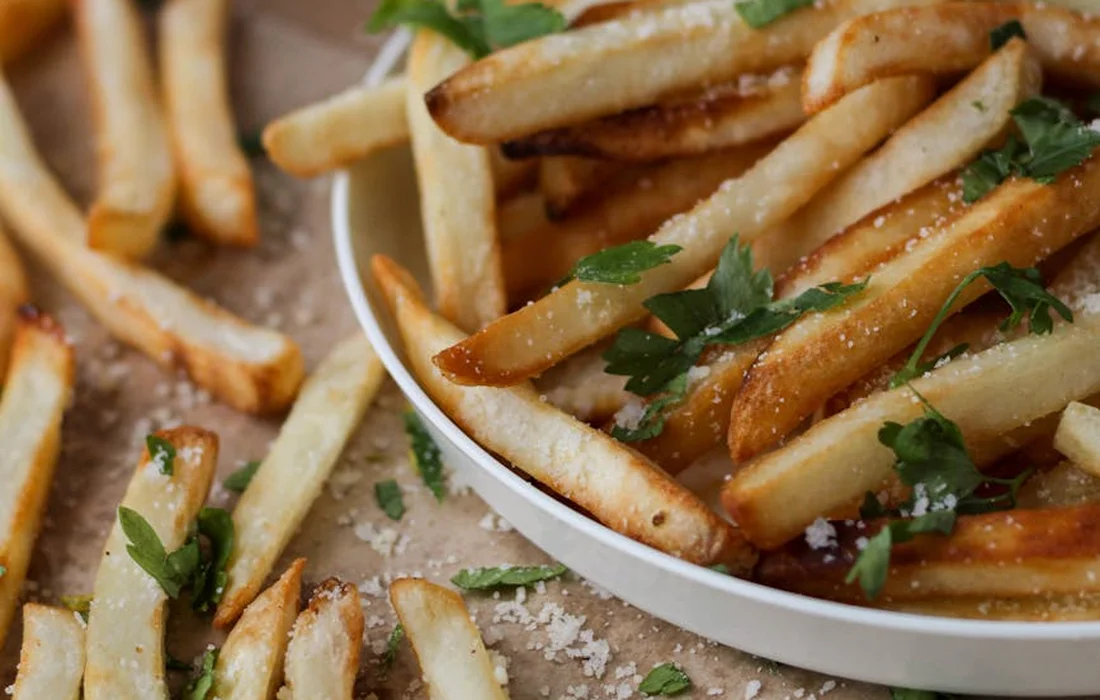 Golden-brown french fries sprinkled with parsley on a white plate.