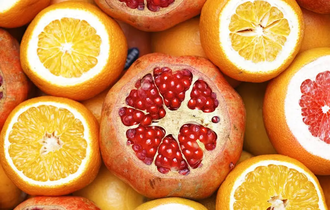 Close-up of a pomegranate cut open with exposed seeds surrounded by orange halves and other citrus fruits.