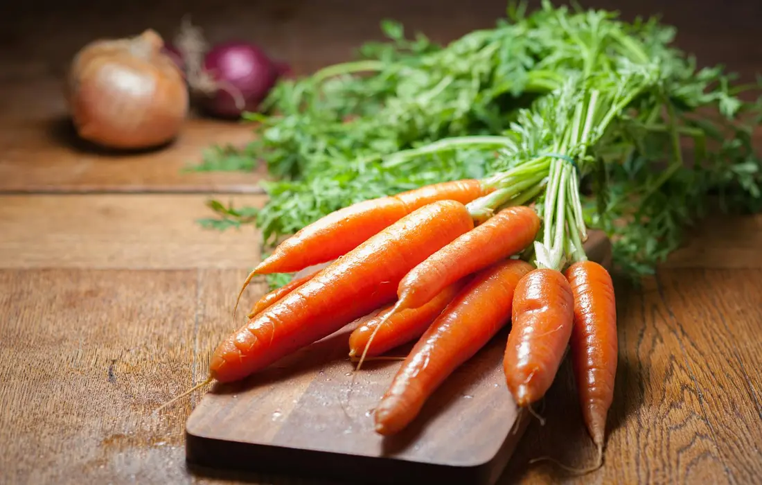 Fresh carrots with green tops on a wooden cutting board, ready for harvesting