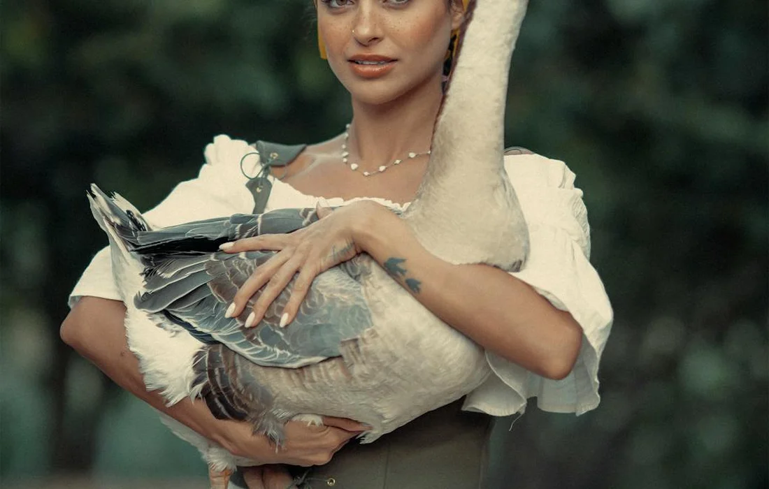 A person wearing a white blouse holds a large white goose outdoors.