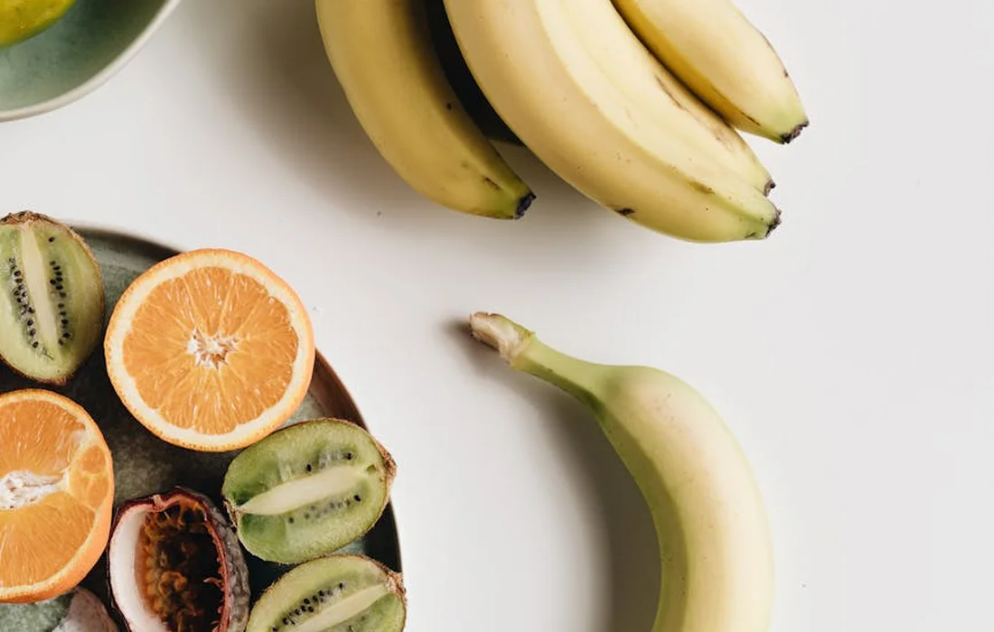 Assorted fruits on a white surface: orange halves, kiwi slices, and bananas.