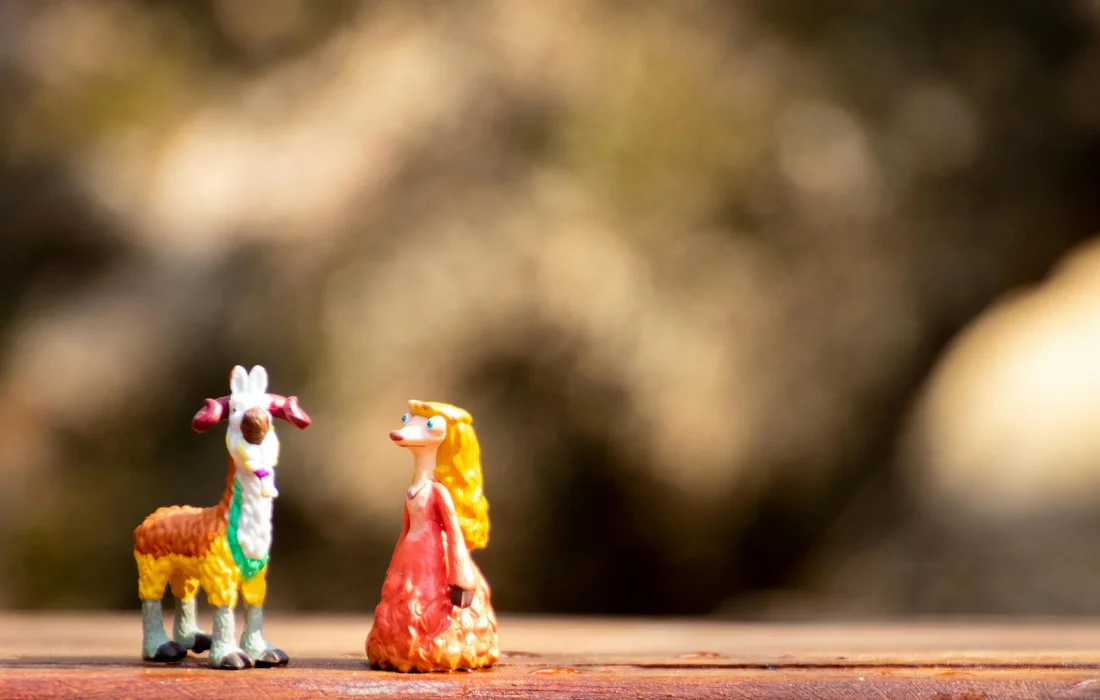 Two small toy figurines, a goat and a girl, on a wooden surface with a blurred natural background.