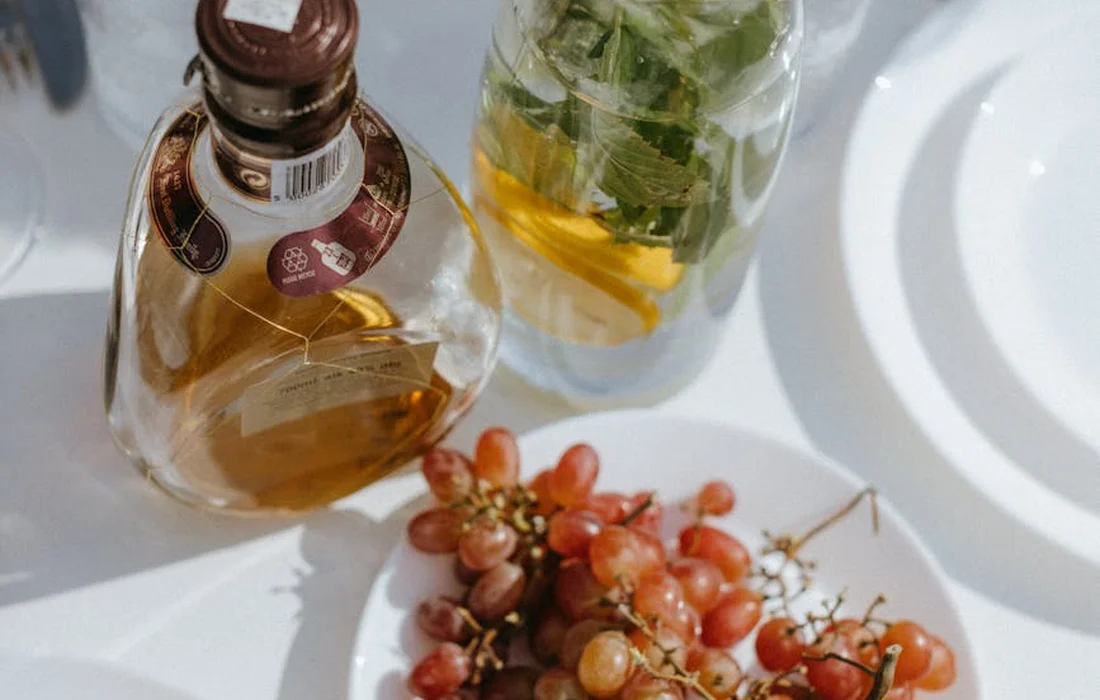 A small cluster of red grapes on a white plate, with two glass bottles of liquids in the background.