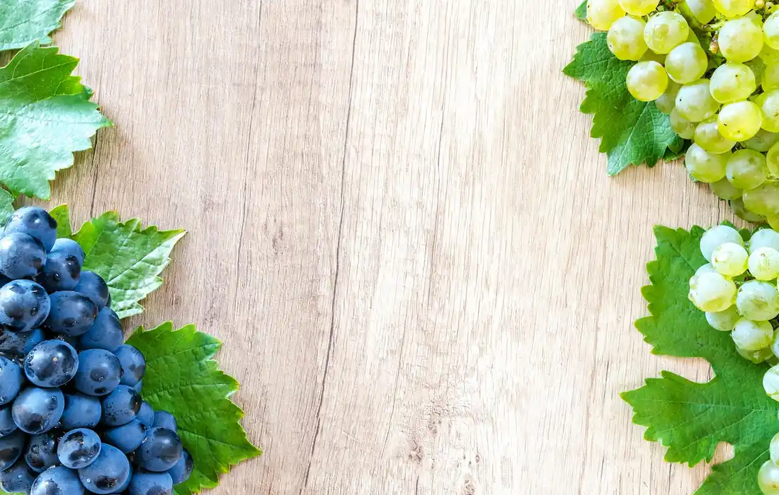 Blue and green grape clusters on a light wooden surface