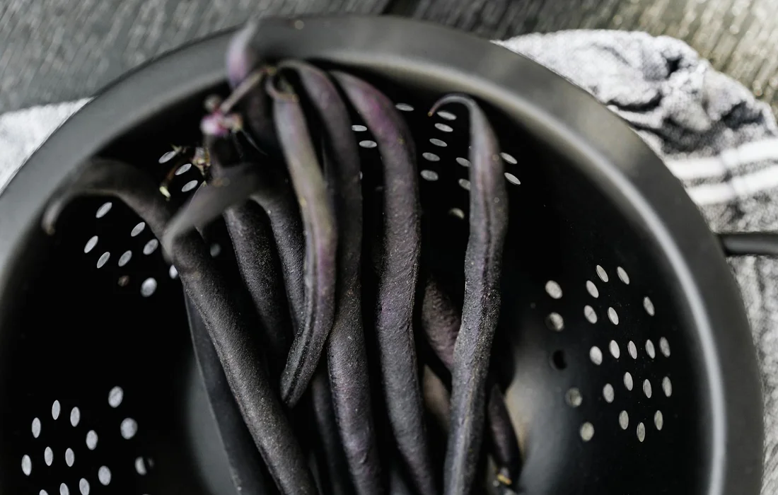 Fresh purple string beans in a black perforated colander