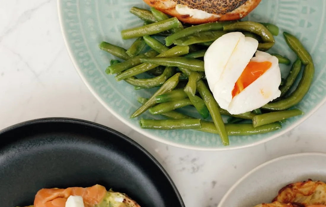 Plate of cooked green beans with a halved boiled egg, with other plates partially visible in the background