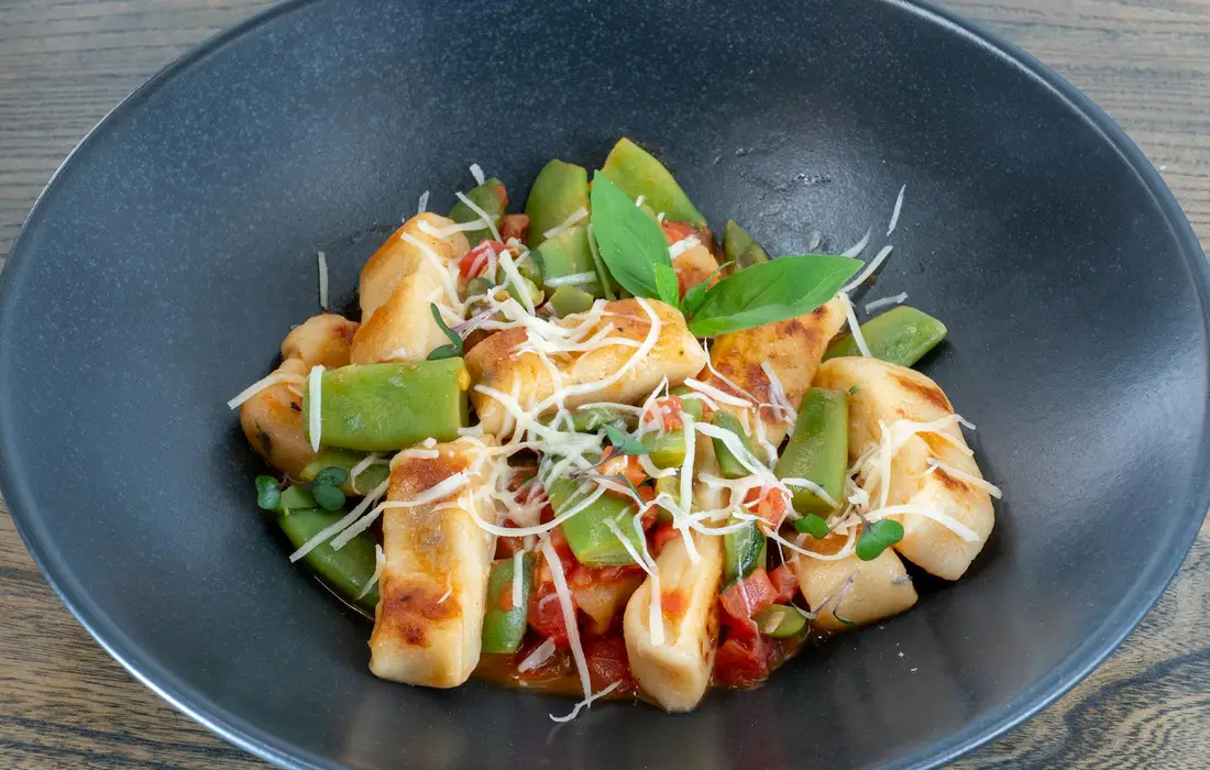 Dish of green beans and vegetables topped with shredded cheese in a dark bowl.