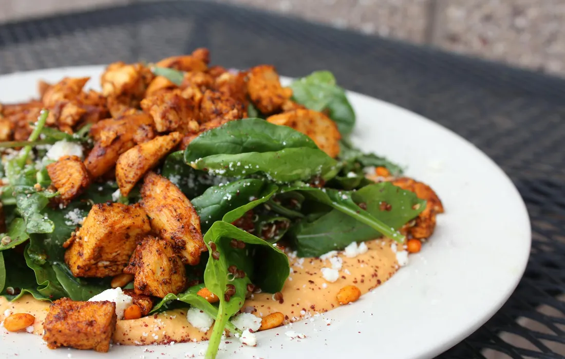Plate of leafy greens topped with cubed, seasoned chicken on a bed of creamy sauce, presented on a white plate.