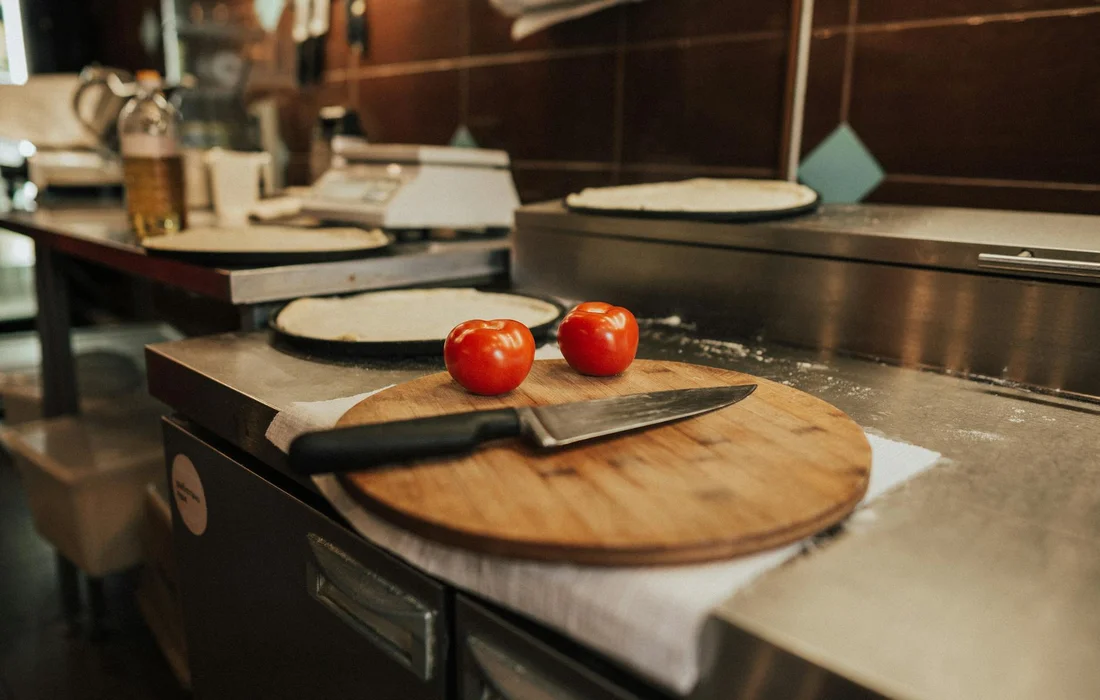 Two cherry tomatoes on a round wooden cutting board with a chef's knife in a kitchen prep area