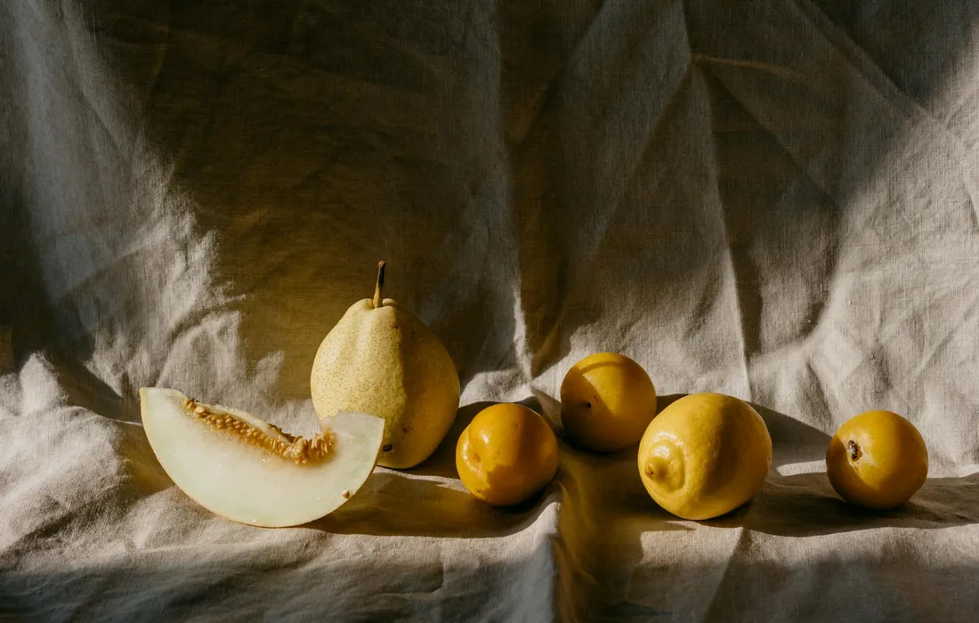Still life of yellow fruits on a textured fabric background, suggesting fruit choices for a guinea pig's diet.