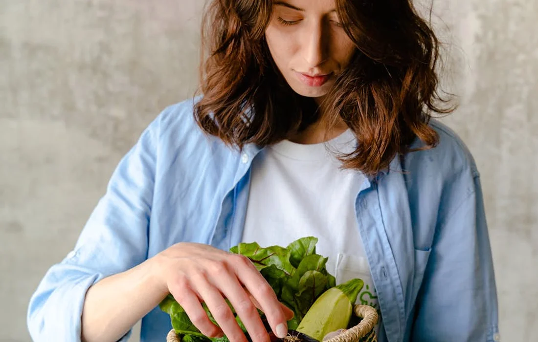 Person in a light blue shirt reaching into a basket of fresh leafy greens