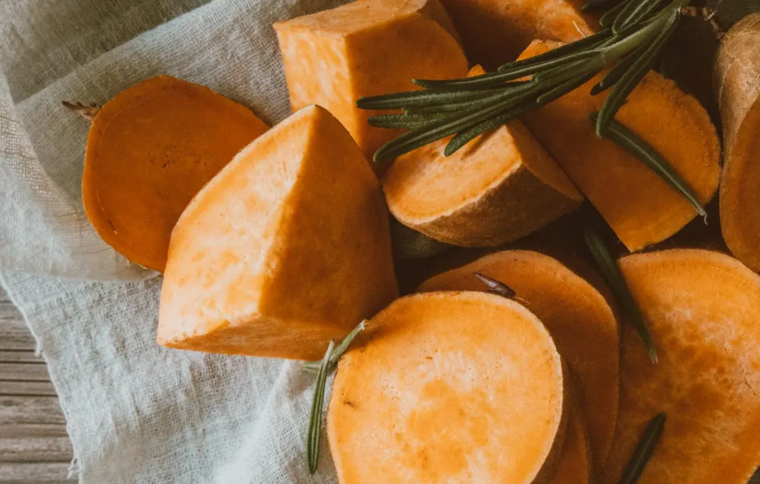 Peeled sweet potato chunks with sprigs of rosemary on a light cloth, ready for rabbit feeding.
