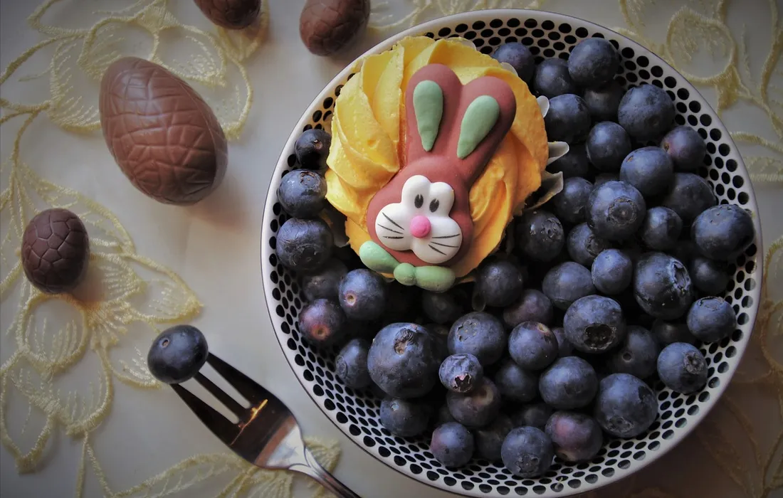 Plate of blueberries with a decorative rabbit-shaped cookie on top, surrounded by a soft lace background