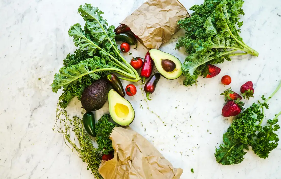 Fresh kale and assorted leafy greens with vegetables spread on a light surface, illustrating a rabbit-friendly daily greens setup.