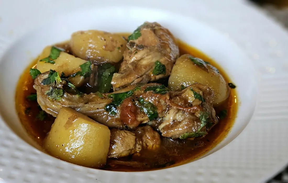 A white bowl of stewed meat and potatoes in a brown sauce, garnished with herbs.