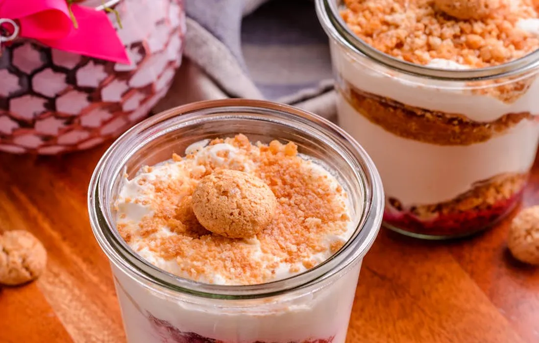 Two glass jars filled with yogurt parfaits, berry layers, and a crumble topping on a wooden surface