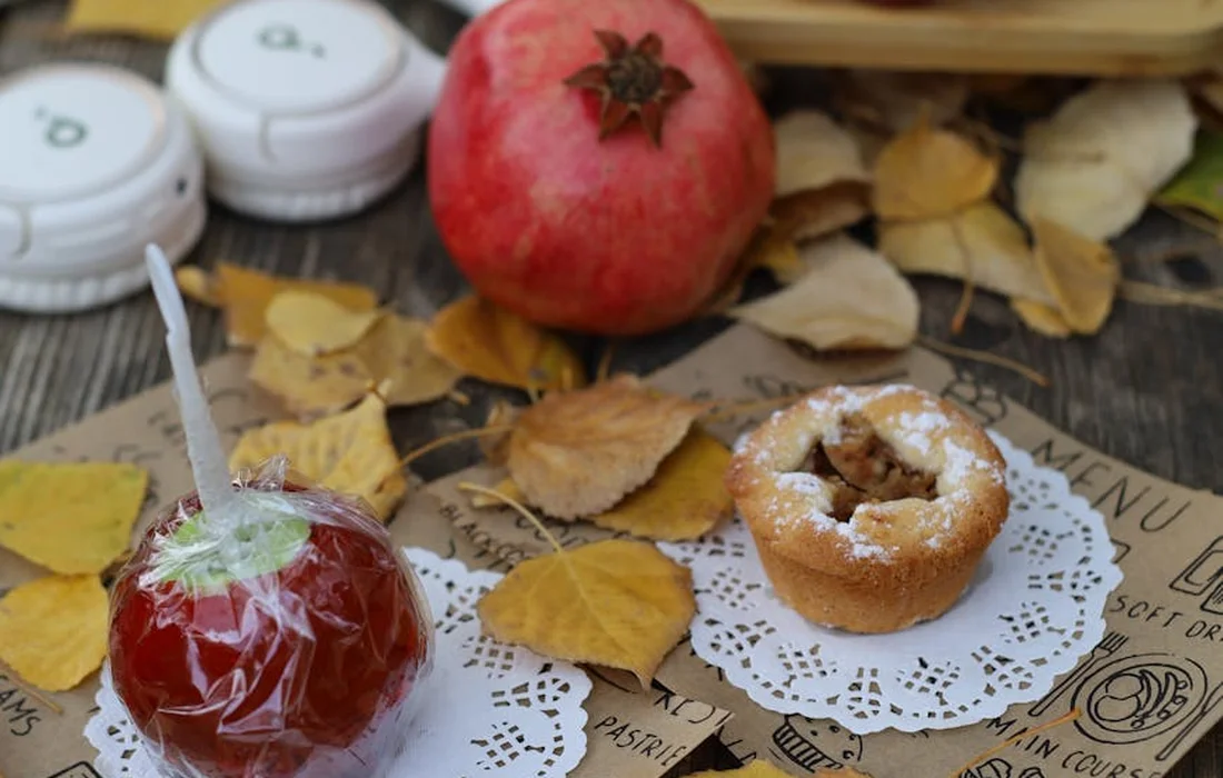 Red candy apple and a pastry ring resting on doily beside autumn leaves on a wooden table, illustrating common human junk foods that should never be fed to horses.